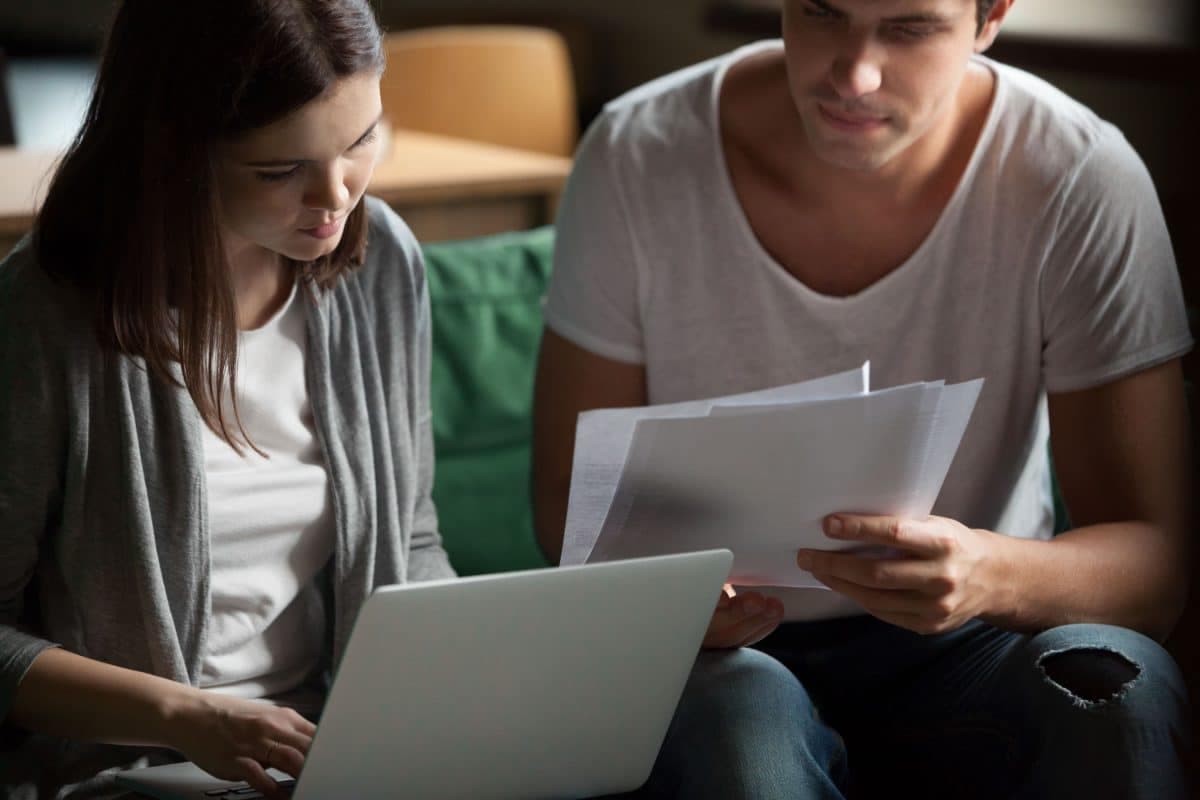 A couple reading paperwork together beside a laptop