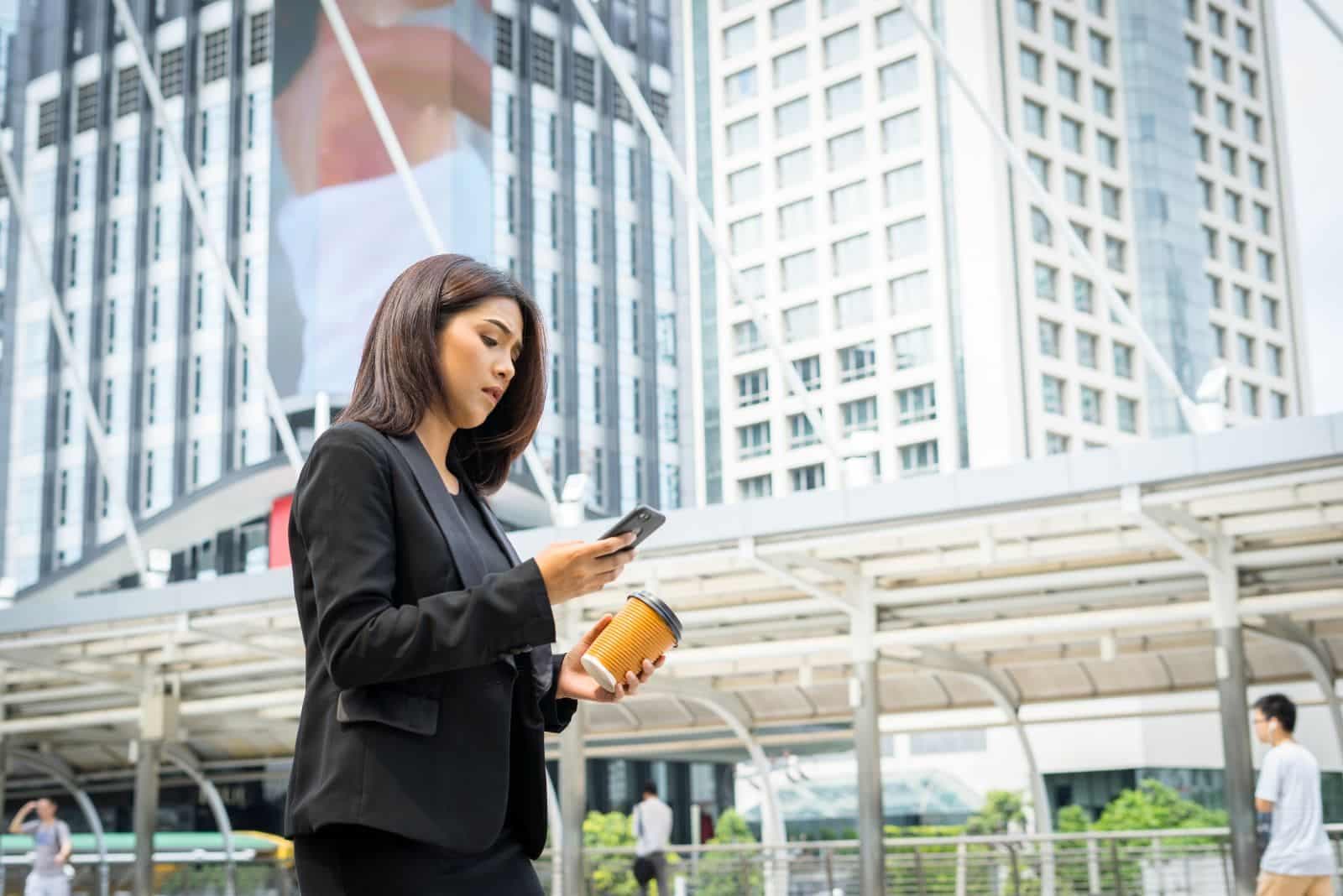A woman checking her phone on a walkway between city office towers