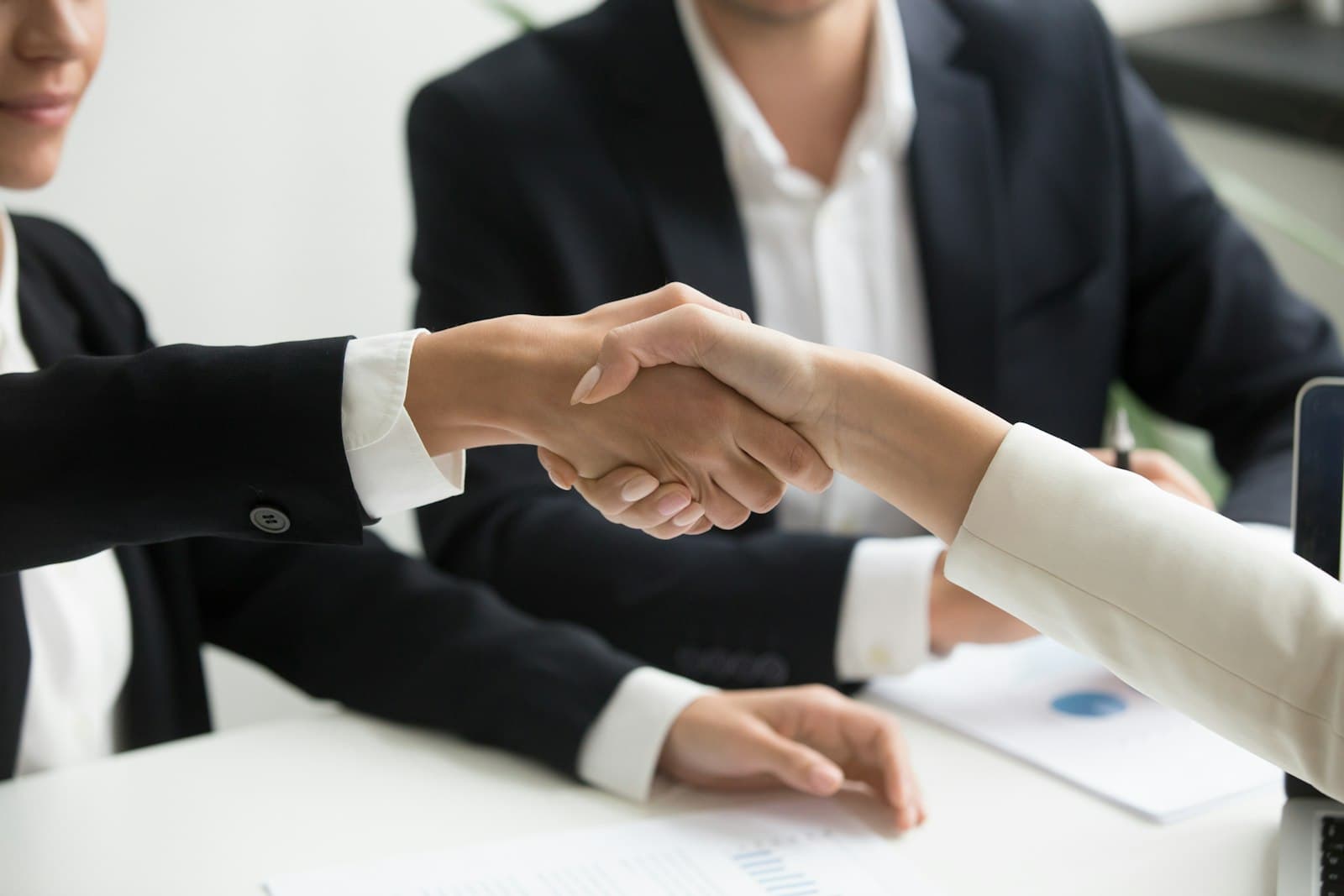 Two people shaking hands across a meeting table
